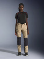 Alpinestars Woman Stella Flex-AST Explorer Pants, Women's Motorcycle Pants, Tan with black panels, worn by a model with a black short-sleeved top and black boots, featuring reinforced knee panels, zippered cargo pockets, and breathable ripstop fabric for warm-weather adventure riding.