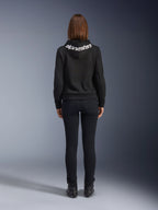 Jeansy Daisy V3 Damskie, Black Rinse, spodnie motocyklowe slim fit, widok z tyłu pokazujący podwyższony stan i kobiecą sylwetkę, zestawione z czarną bluzą z kapturem Alpinestars i czarnymi butami motocyklowymi, miejska odzież casual