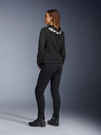 Alpinestars Daisy V3 Women's Riding Denim, damskie spodnie motocyklowe, Rinse Black, widok z tyłu prezentujący dopasowany krój slim fit i podwyższony stan z tyłu, w zestawieniu z czarną bluzą z kapturem Alpinestars i butami motocyklowymi w miejskim stylu