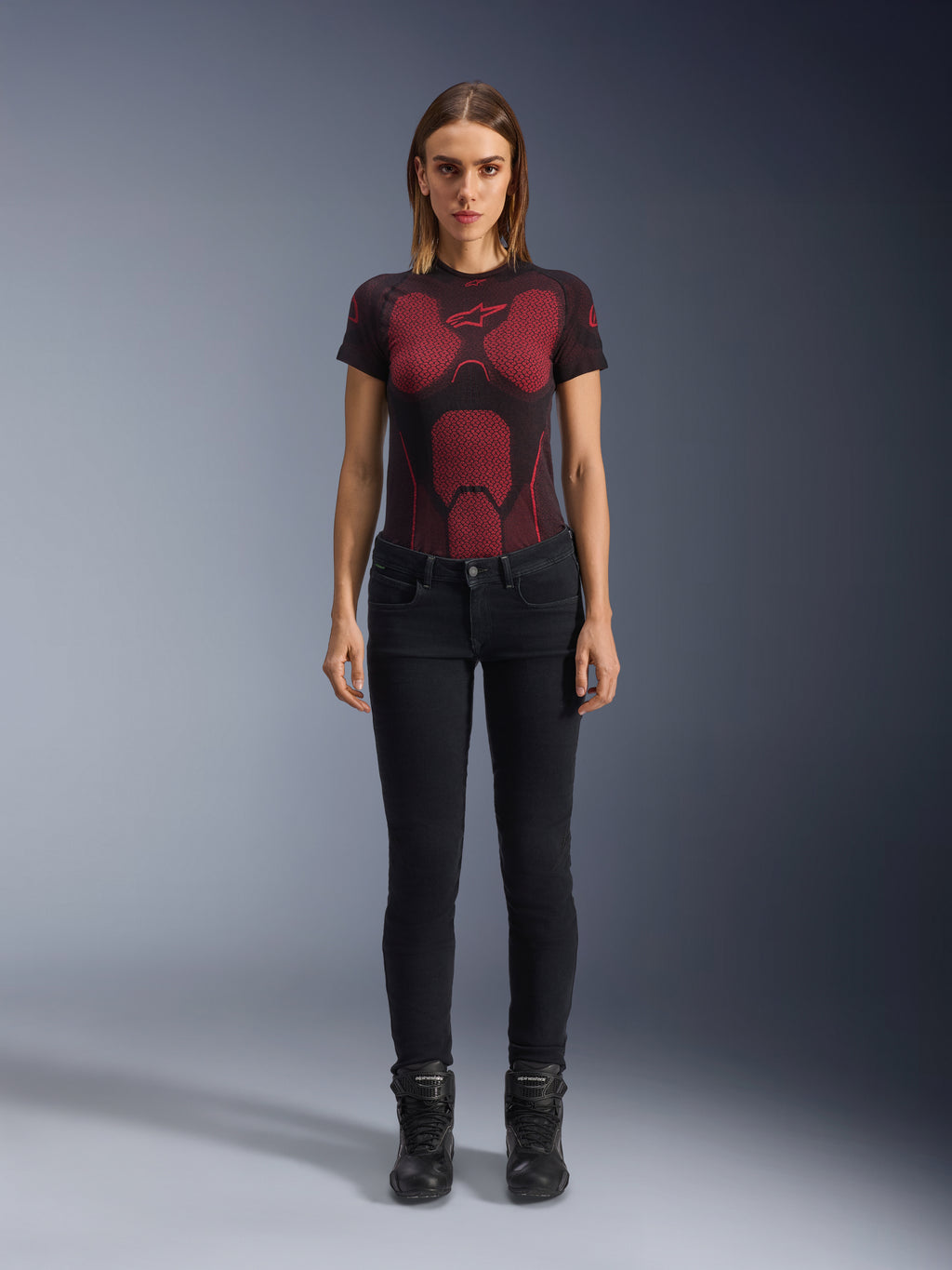 Alpinestars Daisy V3 Women's Riding Denim, Rinse Black, dopasowane spodnie motocyklowe slim-fit, prezentowane przez modelkę w technicznej koszulce z czerwono-czarnym wzorem i czarnych butach motocyklowych, codzienna miejska odzież motocyklowa o kobiecej sylwetce i fasonie z wysokim stanem