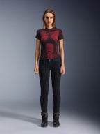 Alpinestars Daisy V3 Women's Riding Denim, Rinse Black, dopasowane spodnie motocyklowe slim-fit, prezentowane przez modelkę w technicznej koszulce z czerwono-czarnym wzorem i czarnych butach motocyklowych, codzienna miejska odzież motocyklowa o kobiecej sylwetce i fasonie z wysokim stanem