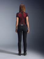 Alpinestars Daisy V3 Women's Riding Denim, Rinse Black, damskie spodnie motocyklowe o kroju slim fit widoczne od tyłu, wysoki stan i tylne kieszenie, w zestawieniu z czerwono-czarną wzorzystą koszulką techniczną i czarnymi butami, miejska odzież motocyklowa dla kobiet