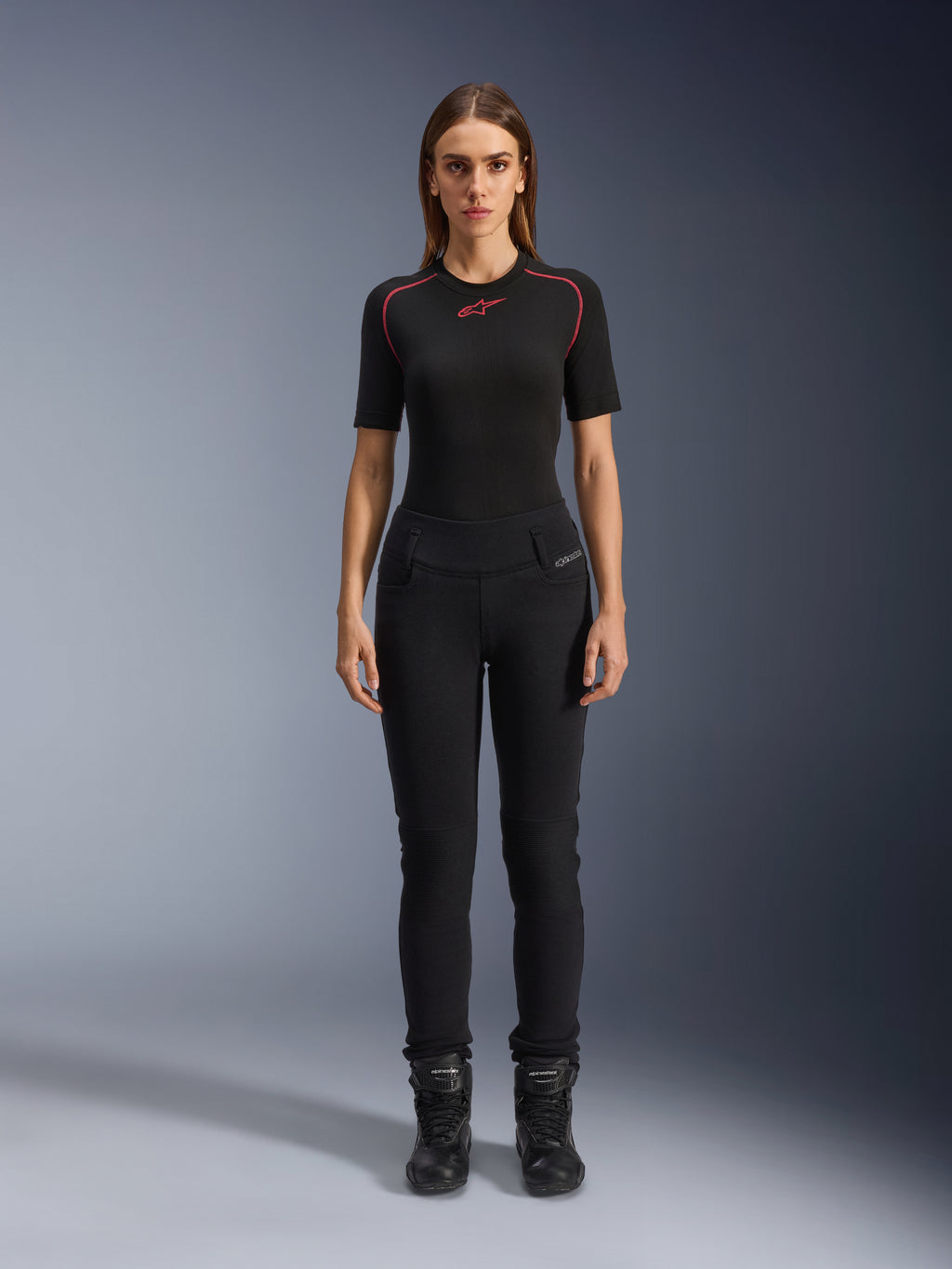 Damskie legginsy Alpinestars Banshee, czarne legginsy motocyklowe, anatomiczny, dopasowany do sylwetki krój, noszone przez modelkę z czarną warstwą bazową i butami motocyklowymi, karbowane panele na kolanach, wysoki stan do jazdy miejskiej.