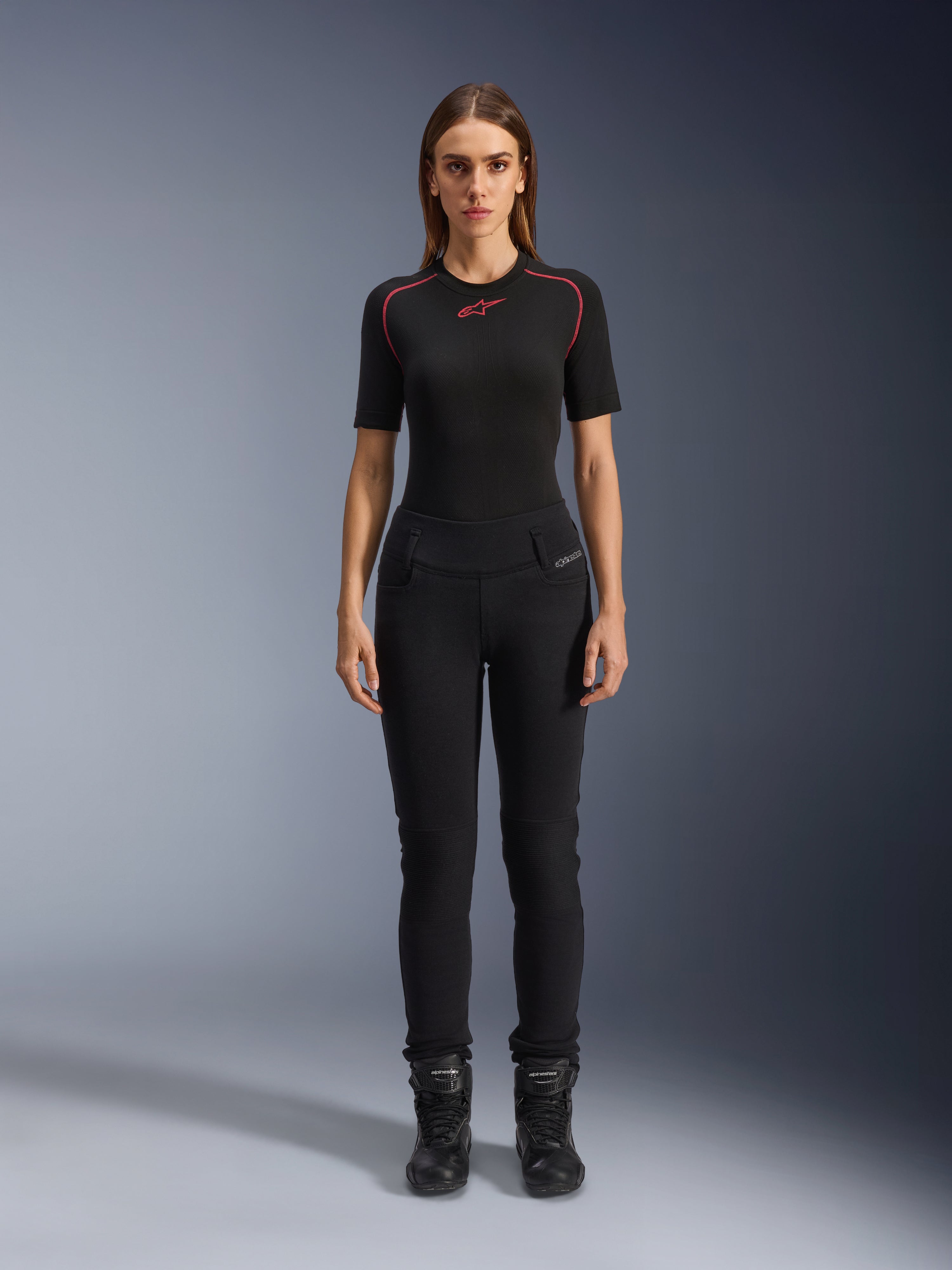 Damskie legginsy Alpinestars Banshee, czarne legginsy motocyklowe, anatomiczny, dopasowany do sylwetki krój, noszone przez modelkę z czarną warstwą bazową i butami motocyklowymi, karbowane panele na kolanach, wysoki stan do jazdy miejskiej.