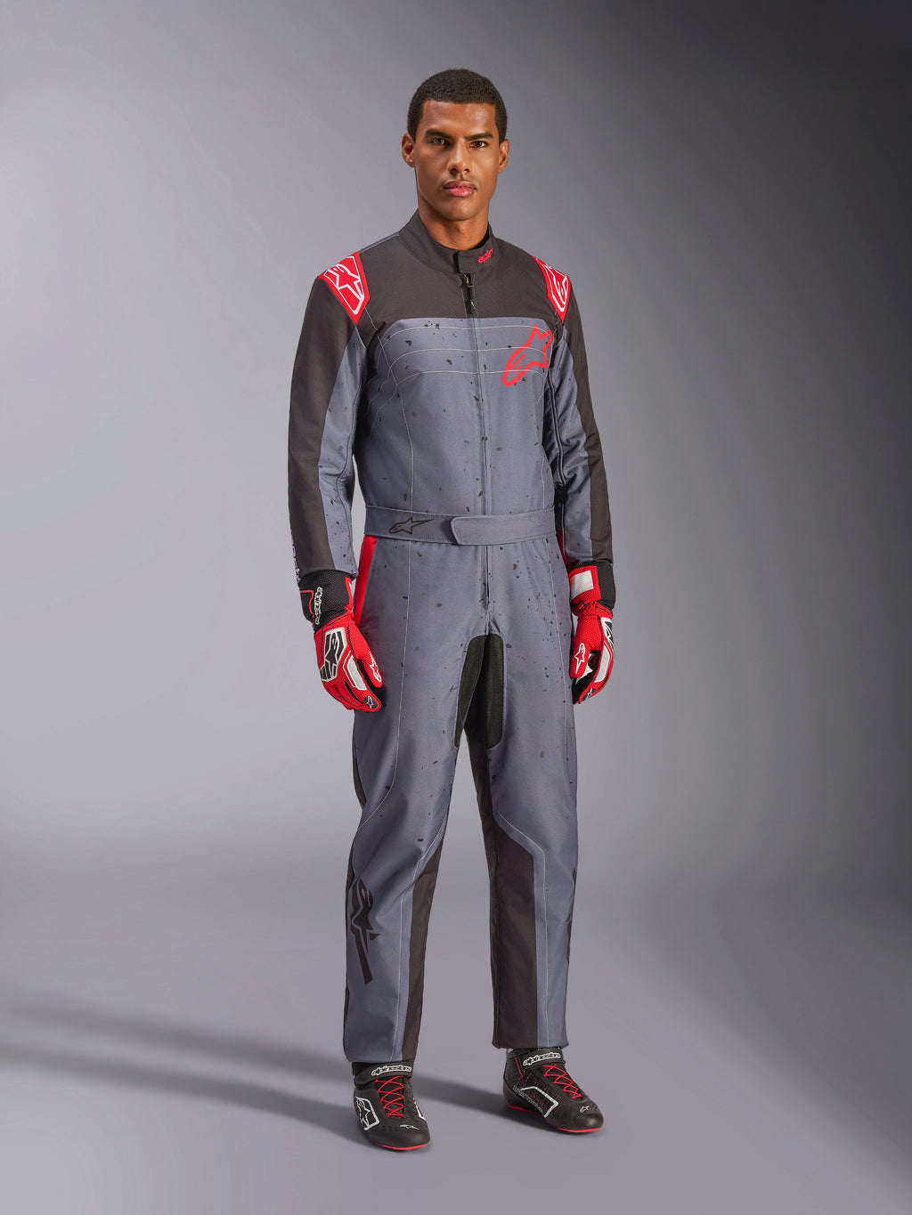 Alpinestars KMX-9 V3 Graphic 6, kombinezon kartingowy, szary i antracytowy z czerwonymi akcentami, unikalna grafika splash na klatce piersiowej i nogawkach, czerwone rękawice wyścigowe, czarne buty kartingowe, ujęcie całej sylwetki w studiu