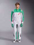 Alpinestars KMX-9 V3 Graphic 6 Suit, biało-zielono-czerwony, jednoczęściowy kombinezon kartingowy z czarnym wzorem graficznym typu splatter, zielone panele na rękawach i nogawkach, czerwone logo Alpinestars na piersi, noszony z pasującymi rękawicami i butami wyścigowymi.