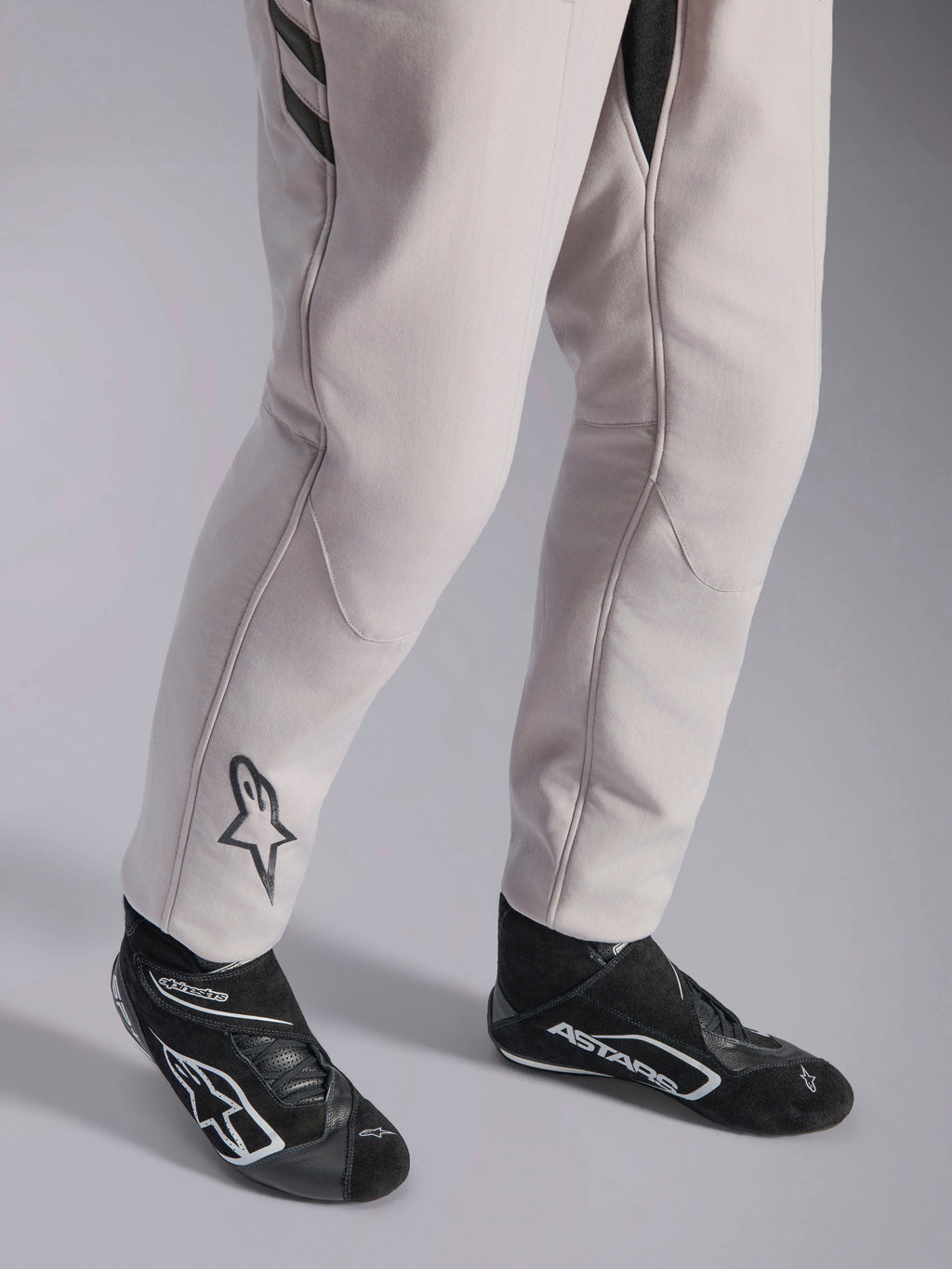 Alpinestars GP Race V3 Suit FIA, samochodowy kombinezon wyścigowy Silver Anthracite, zbliżenie na dolną część nogawek i czarne buty wyścigowe, czarne logo Astars na łydce, profesjonalny sprzęt do sportów motorowych z żebrowanymi mankietami