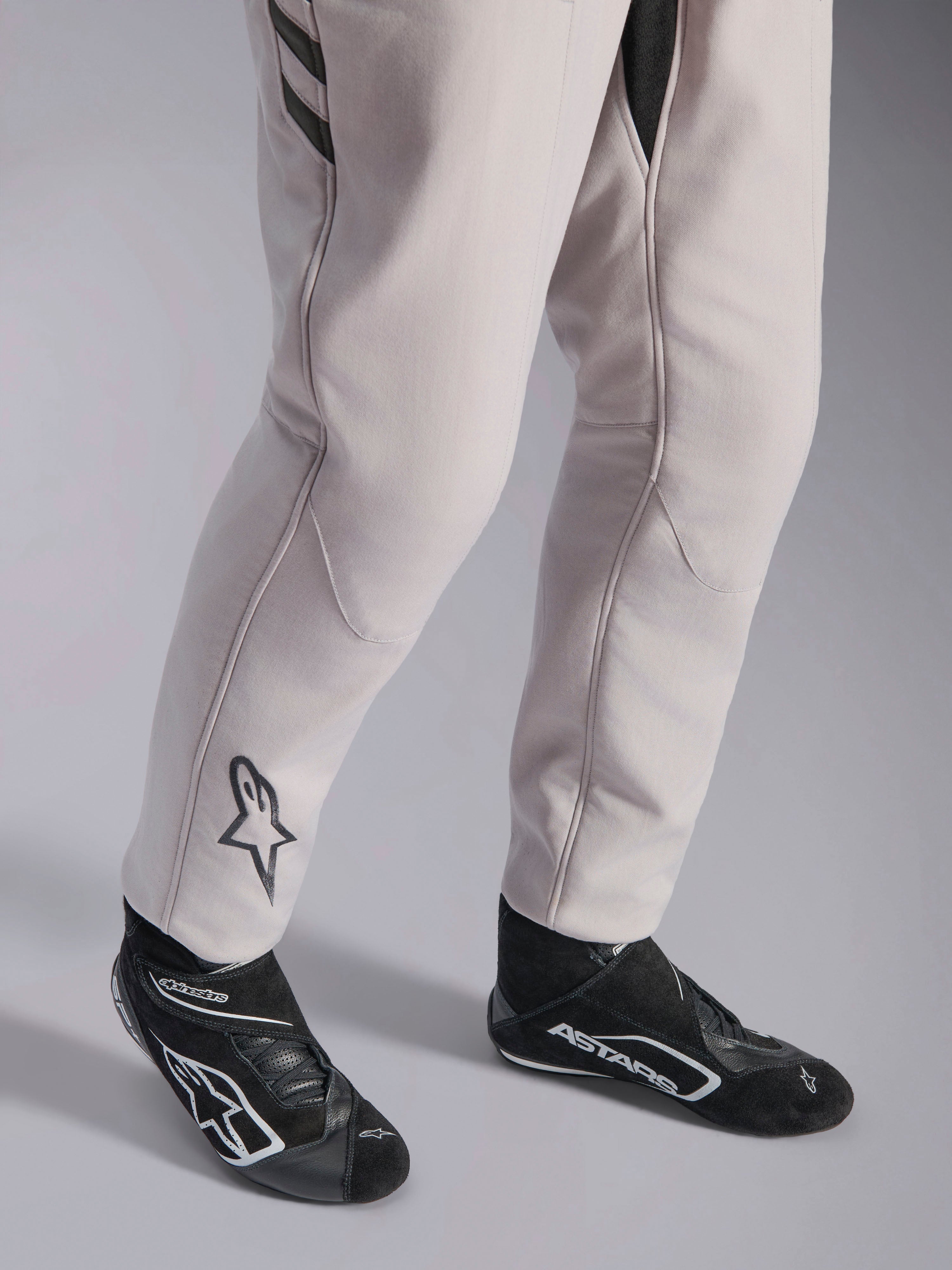 Alpinestars GP Race V3 Suit FIA, samochodowy kombinezon wyścigowy Silver Anthracite, zbliżenie na dolną część nogawek i czarne buty wyścigowe, czarne logo Astars na łydce, profesjonalny sprzęt do sportów motorowych z żebrowanymi mankietami