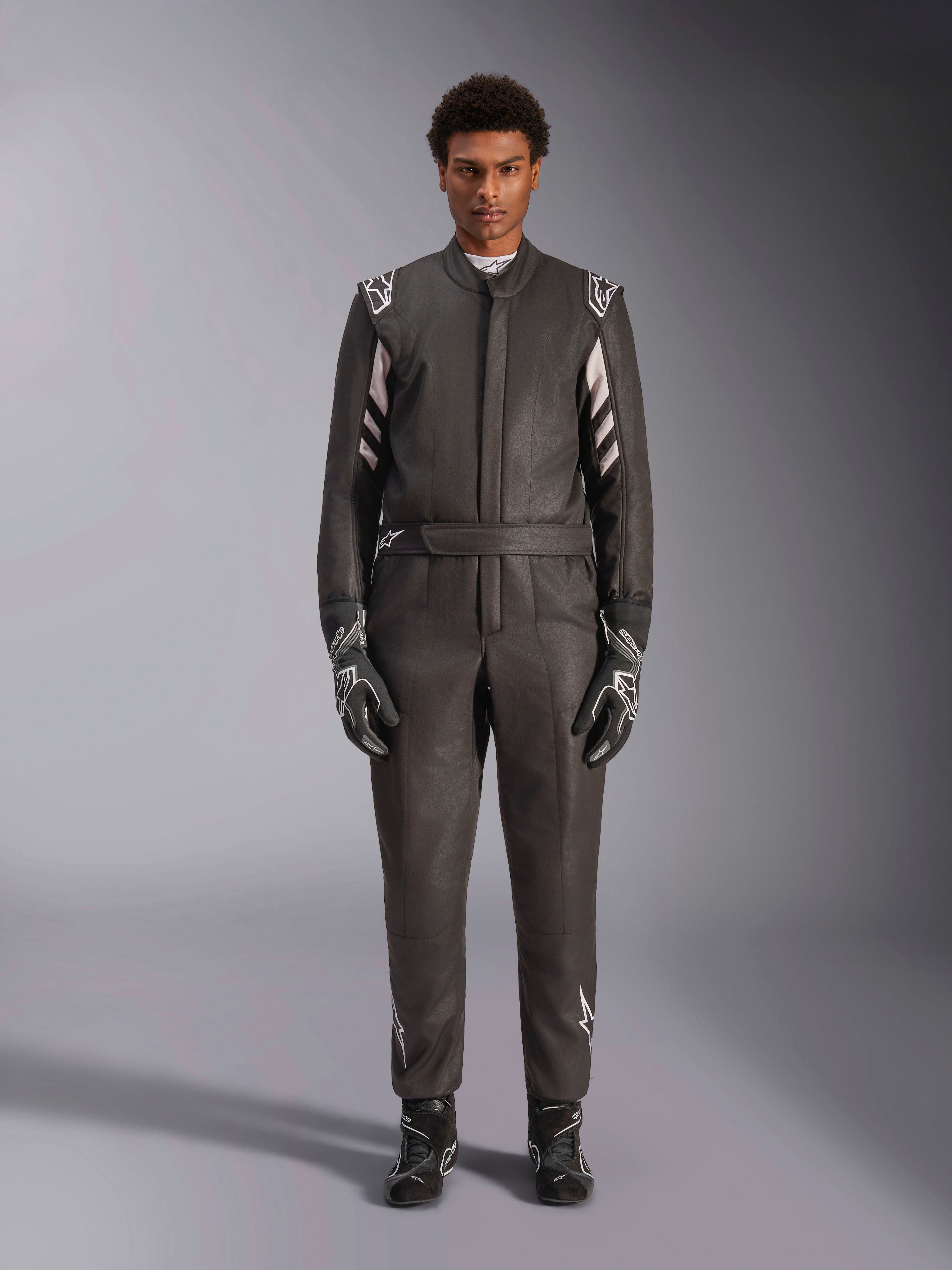 Alpinestars GP Race V3 Suit FIA, kombinezon samochodowy, czarno-srebrny, widok z przodu na kierowcę w pełnym stroju wyścigowym z rękawicami i butami, profesjonalny design motorsportowy z logo Alpinestars na ramionach i pasku
