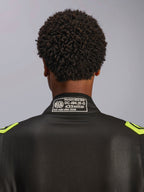 Alpinestars GP Race V3 Suit FIA, czarny i żółty fluo, zbliżenie na tylną część kołnierza z widoczną etykietą certyfikacji FIA 8856-2018, profesjonalny samochodowy kombinezon wyścigowy