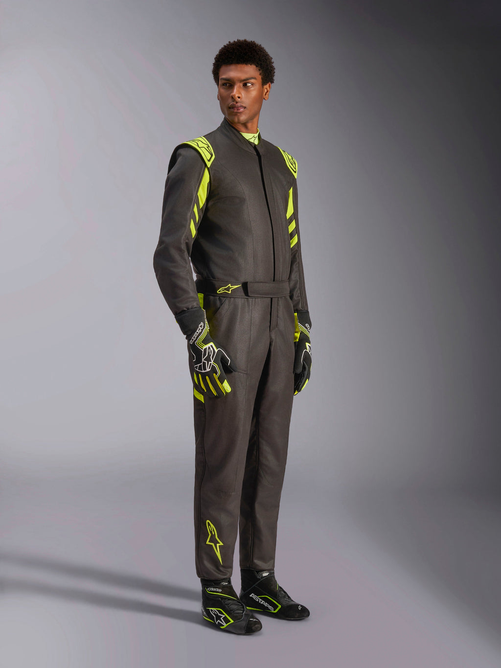 Alpinestars GP Race V3 Suit FIA, kombinezon samochodowy, czarno-żółty fluo, prezentowany przez modela z dopasowanymi rękawicami i butami wyścigowymi, jaskrawe żółte akcenty na ramionach i nogawkach, profesjonalna odzież motorsportowa