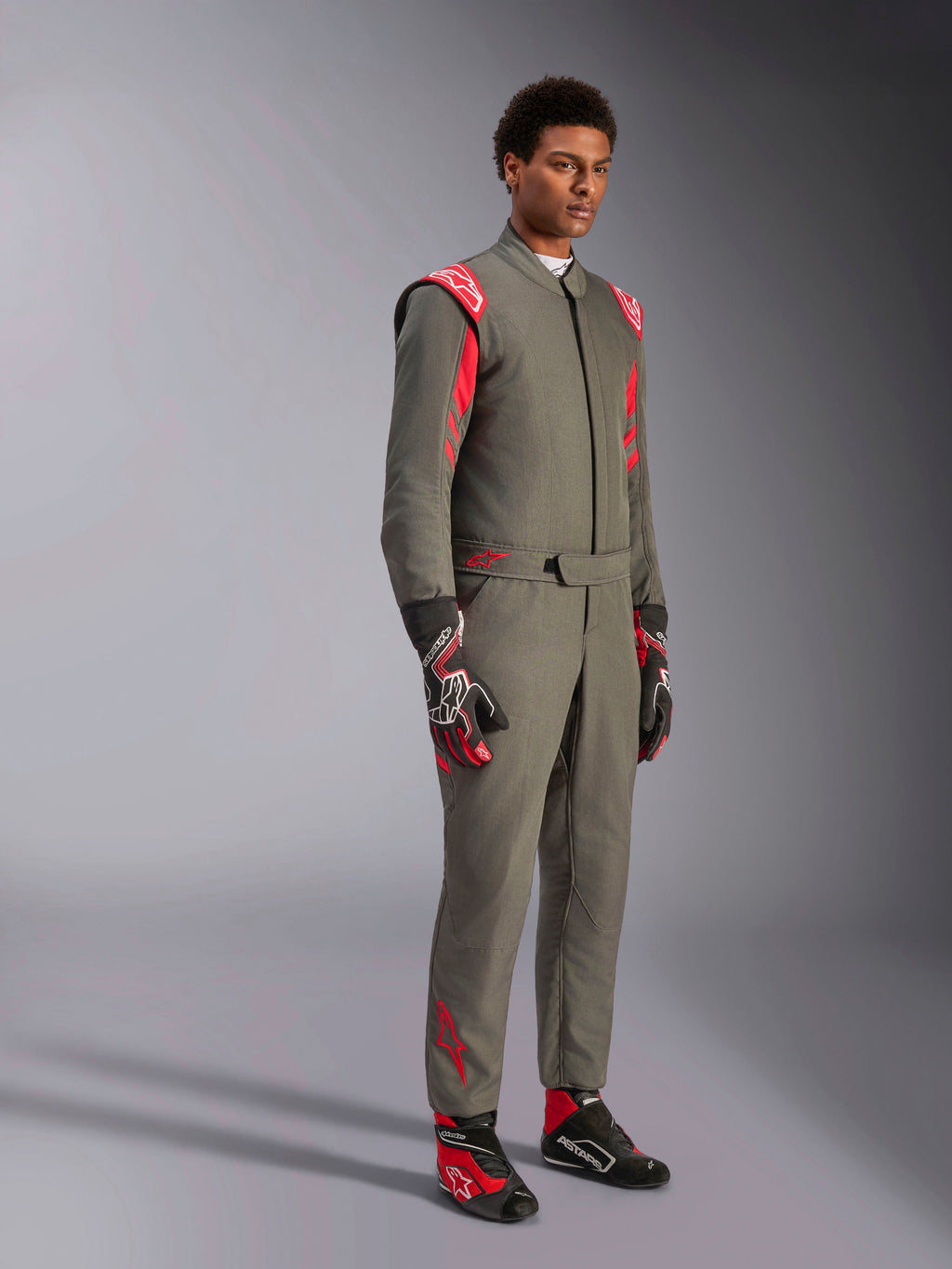 Alpinestars GP Race V3 Suit FIA, antracytowo-czerwony kombinezon wyścigowy, zestawiony z dopasowanymi rękawicami i butami wyścigowymi, z czerwonymi epoletami na ramionach i brandingiem, smukła dwuwarstwowa konstrukcja techniczna do sportów motorowych