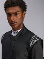 Kombinezon Alpinestars Hypertech V3, samochodowy kombinezon wyścigowy Black Dark Shadow, zbliżenie na modela, srebrne logo na ramionach, wysoki kołnierz z białym półgolfem Alpinestars, profesjonalna odzież ochronna do sportów motorowych