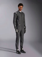 Kombinezon Alpinestars Hypertech V3, samochodowy kombinezon wyścigowy, kolor czarny i Dark Shadow, prezentowany przez modela z dopasowanymi czarnymi rękawicami i butami wyścigowymi, sportowy, dopasowany krój, widoczne logo Alpinestars i jasnoszare akcenty, profesjonalna odzież ochronna do sportów motorowych