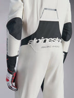 Kombinezon Alpinestars Hypertech V3, biało-czarno-srebrny kombinezon samochodowy, widok z tyłu z dużym czarnym logo „alpinestars” i napisem „RACING AHEAD”, czarne panele rozciągliwe na łokciach i w okolicy lędźwiowej, profesjonalna odzież ochronna do sportów motorowych
