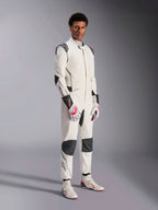 Męski model w kombinezonie Alpinestars Hypertech V3, biały z czarnymi i srebrnymi akcentami, profesjonalny strój do wyścigów samochodowych z czarnymi panelami na ramionach i kolanach, biało-czerwone rękawice wyścigowe i białe buty wyścigowe