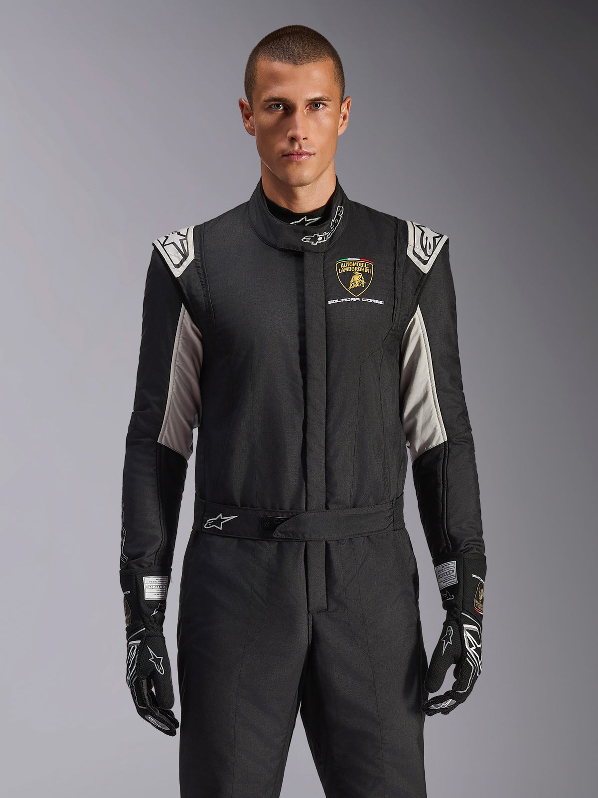 Alpinestars Limited Edition Lamborghini GP Tech V4 Suit, professional racing suit in black with silver and gold accents, featuring the Automobili Lamborghini Squadra Corse shield on the chest, worn by a model with matching black racing gloves.