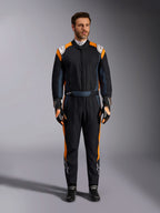 Alpinestars GP Pro Comp V2 FIA Suit, Black Asphalt and Orange Fluo auto racing suit, male model wearing full protective gear with matching racing gloves and shoes, features white Alpinestars logos and vibrant orange side panels, professional motorsport apparel