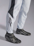 Alpinestars GP Pro Comp V2 FIA, kombinezon wyścigowy, szary i czarny, logo gwiazdy na nogawce i czarne buty wyścigowe.
