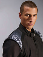 Mężczyzna w kombinezonie Alpinestars KMX-5 V3, kombinezon kartingowy Black Dark Shadow, zbliżenie na klatkę piersiową i ramiona, szare akcenty i białe logo Astars, profesjonalna odzież ochronna do sportów motorowych