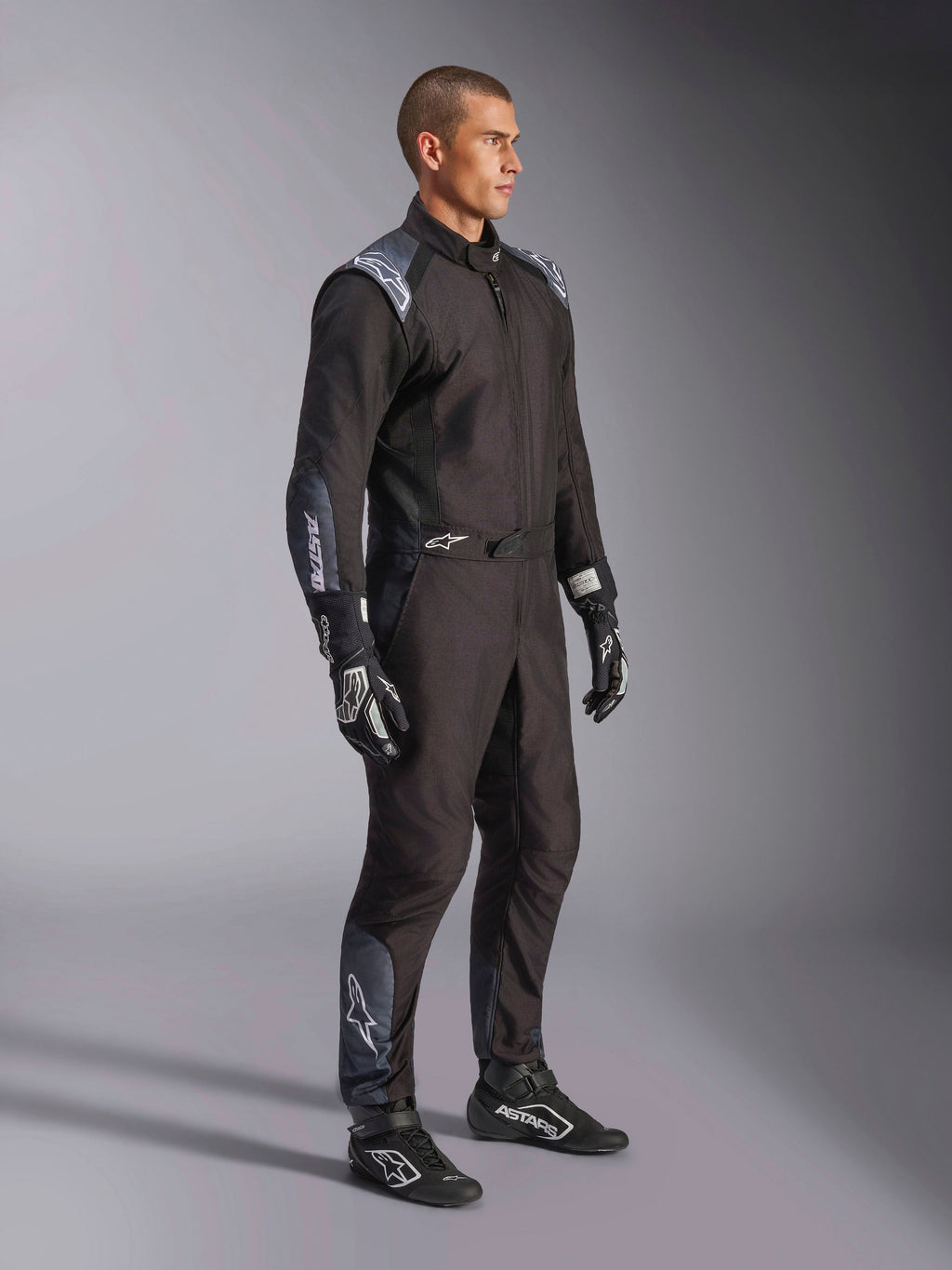 Kombinezon Alpinestars KMX-5 V3, kombinezon kartingowy w kolorze Black Dark Shadow, zestawiony z pasującymi czarnymi rękawicami i butami wyścigowymi, laserowo wycinane perforacje i panele z siatki technicznej, smukła dwuwarstwowa konstrukcja z białym logo dla profesjonalnego motorsportu.