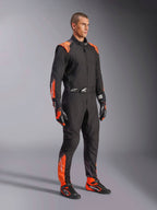 Alpinestars KMX-5 V3, męski jednoczęściowy kombinezon kartingowy, czarny i pomarańczowy fluo, tekstylny, certyfikat FIA klasa 1, noszony przez modela.