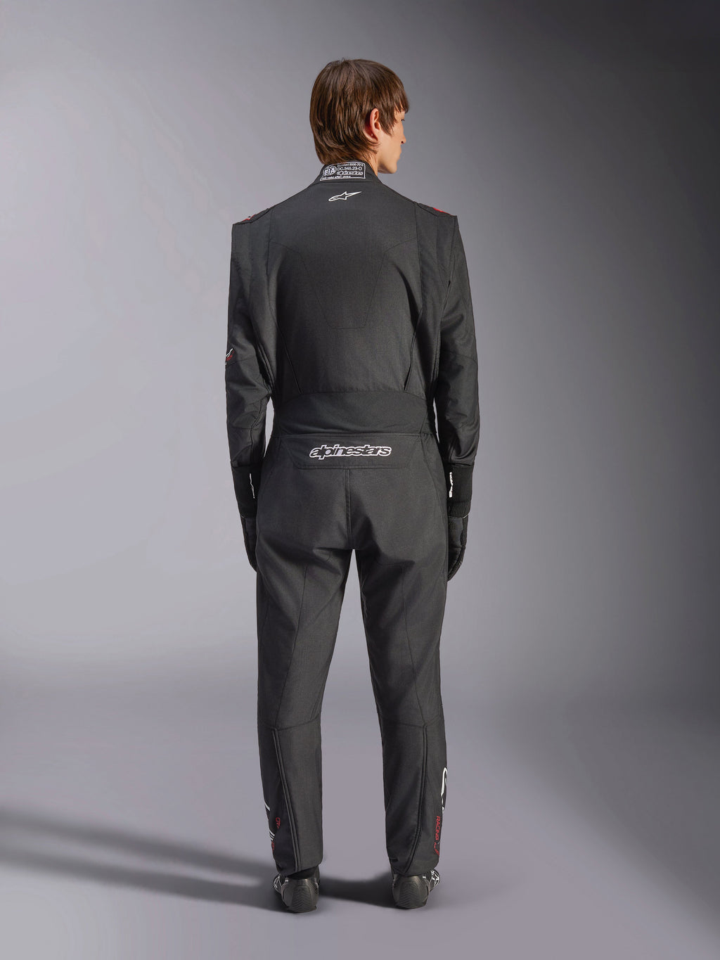 Alpinestars GP Tech V4 Suit, samochodowy kombinezon wyścigowy, czarno-biały, widok z tyłu przedstawiający białe logo Alpinestars oraz certyfikację FIA na kołnierzu, smukłe ergonomiczne dopasowanie dla ochrony profesjonalnego kierowcy