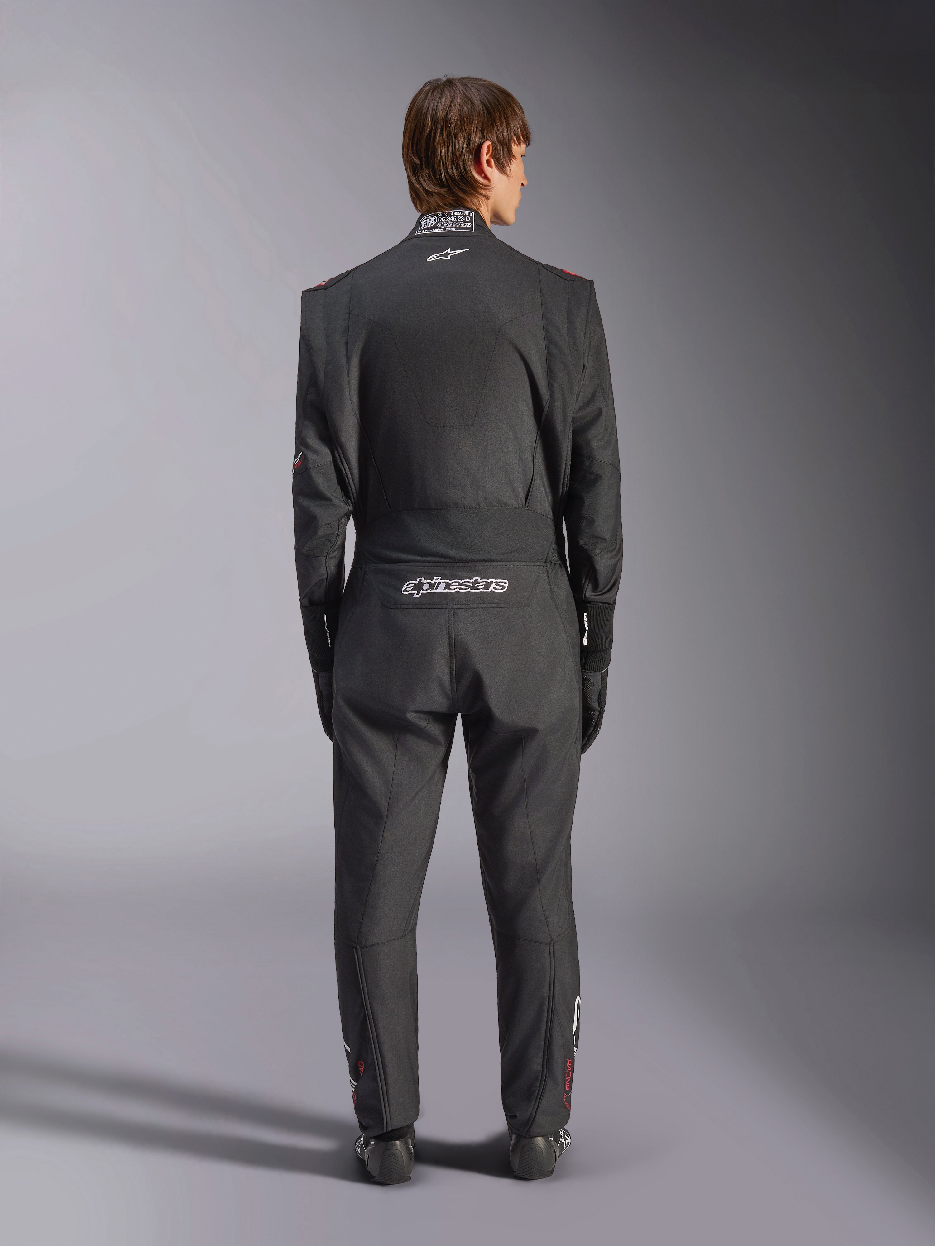 Alpinestars GP Tech V4 Suit, samochodowy kombinezon wyścigowy, czarno-biały, widok z tyłu przedstawiający białe logo Alpinestars oraz certyfikację FIA na kołnierzu, smukłe ergonomiczne dopasowanie dla ochrony profesjonalnego kierowcy