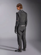 Kombinezon Alpinestars GP Tech V4, kombinezon samochodowy, czarny z białymi akcentami, widok z tyłu na modela ubranego w kombinezon, rękawice i buty wyścigowe, z białym logo na dole pleców i nogawce, profesjonalna odzież ochronna do sportów motorowych