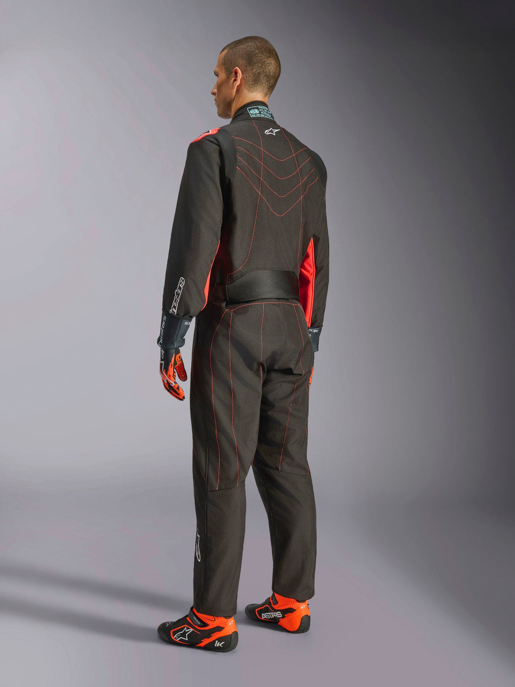 Alpinestars KMX-9 V3 Suit, kombinezon kartingowy, czarny i czerwony fluo, widok z tyłu, z czerwonymi kontrastowymi przeszyciami i fluorescencyjnymi panelami bocznymi, noszony z rękawicami wyścigowymi i butami kartingowymi, profesjonalna odzież motorsportowa