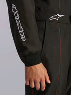Zbliżenie na kombinezon Alpinestars KMX-9 V3 w kolorze czarnym i czerwonym fluo, z białym haftowanym logo Alpinestars na rękawie, dzianinowym mankietem oraz pasem w talii z logo Astars i czerwonymi kontrastowymi szwami.
