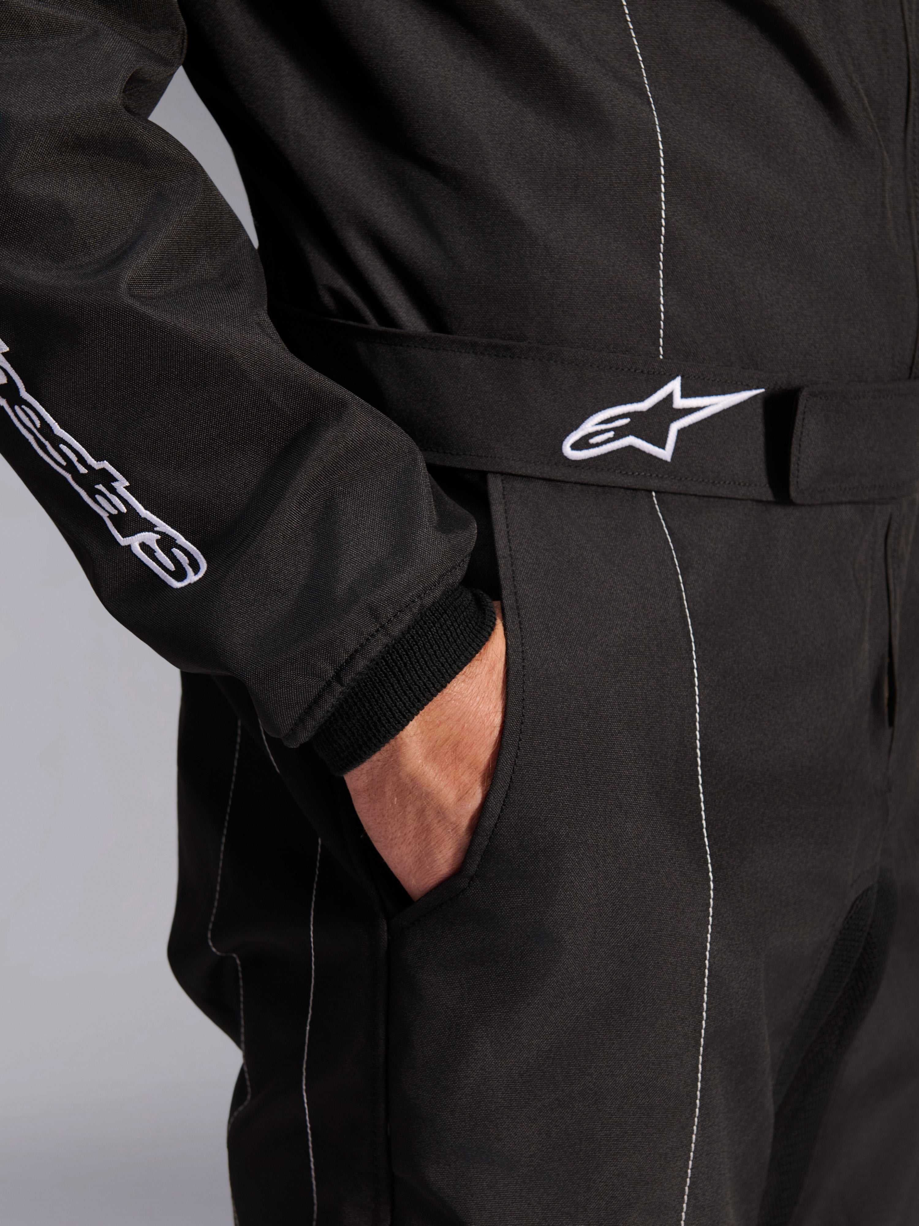 Alpinestars KMX-9 V3 Suit, Black and White, close-up view of adjustable waist belt with embroidered logo, side pocket, white contrast stitching on black fabric, technical karting suit detail