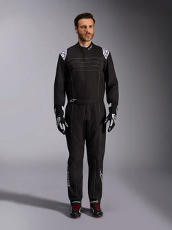 Kombinezon Alpinestars KMX-9 V3, czarno-biały kombinezon kartingowy, widok całej sylwetki na modelu, białe logo na ramionach i akcenty, czarno-białe rękawice wyścigowe i czarne buty z czerwonymi sznurowadłami, krój athletic-regular, profesjonalna odzież kartingowa