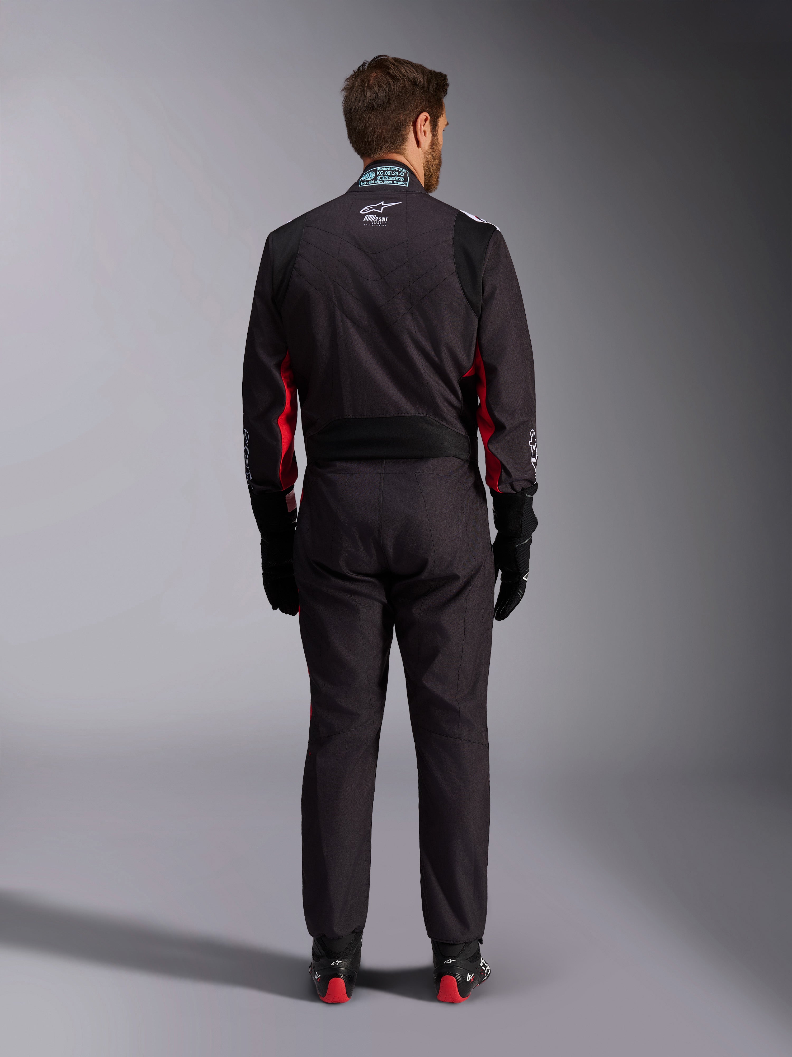 Alpinestars KMX-9 V3 Graphic 3 Suit, kombinezon kartingowy, czarno-czerwony, widok z tyłu przedstawiający elastyczny panel lędźwiowy i metkę z certyfikatem FIA na kołnierzu, zestawiony z czarnymi rękawicami wyścigowymi i butami z czerwonymi akcentami