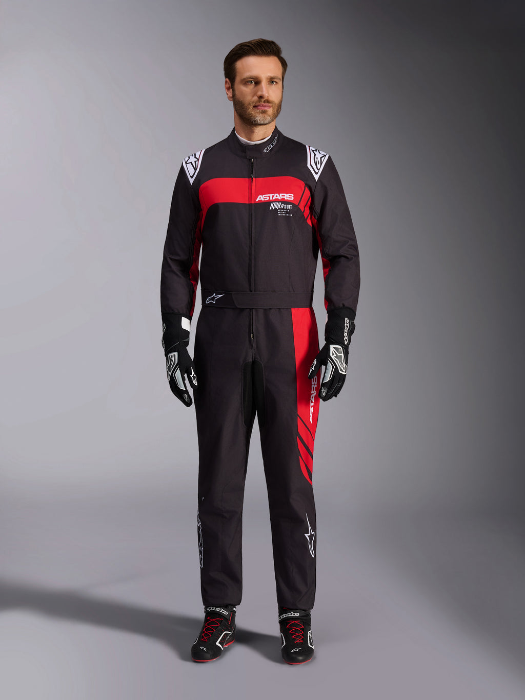 Alpinestars KMX-9 V3 Graphic 3 Suit, kombinezon kartingowy, czarno-czerwony, widok od przodu na modelu, wyraziste czerwone panele graficzne i białe logo, czarne rękawice i buty wyścigowe, profesjonalna odzież do sportów motorowych