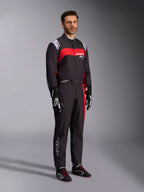 Męski model w kombinezonie Alpinestars KMX-9 V3 Graphic 3, kombinezon kartingowy, czarno-czerwony, z białymi epoletami na ramionach i czerwonym logo na piersi, czarne rękawice wyścigowe i buty z czerwonymi sznurowadłami, profesjonalna odzież motorsportowa.