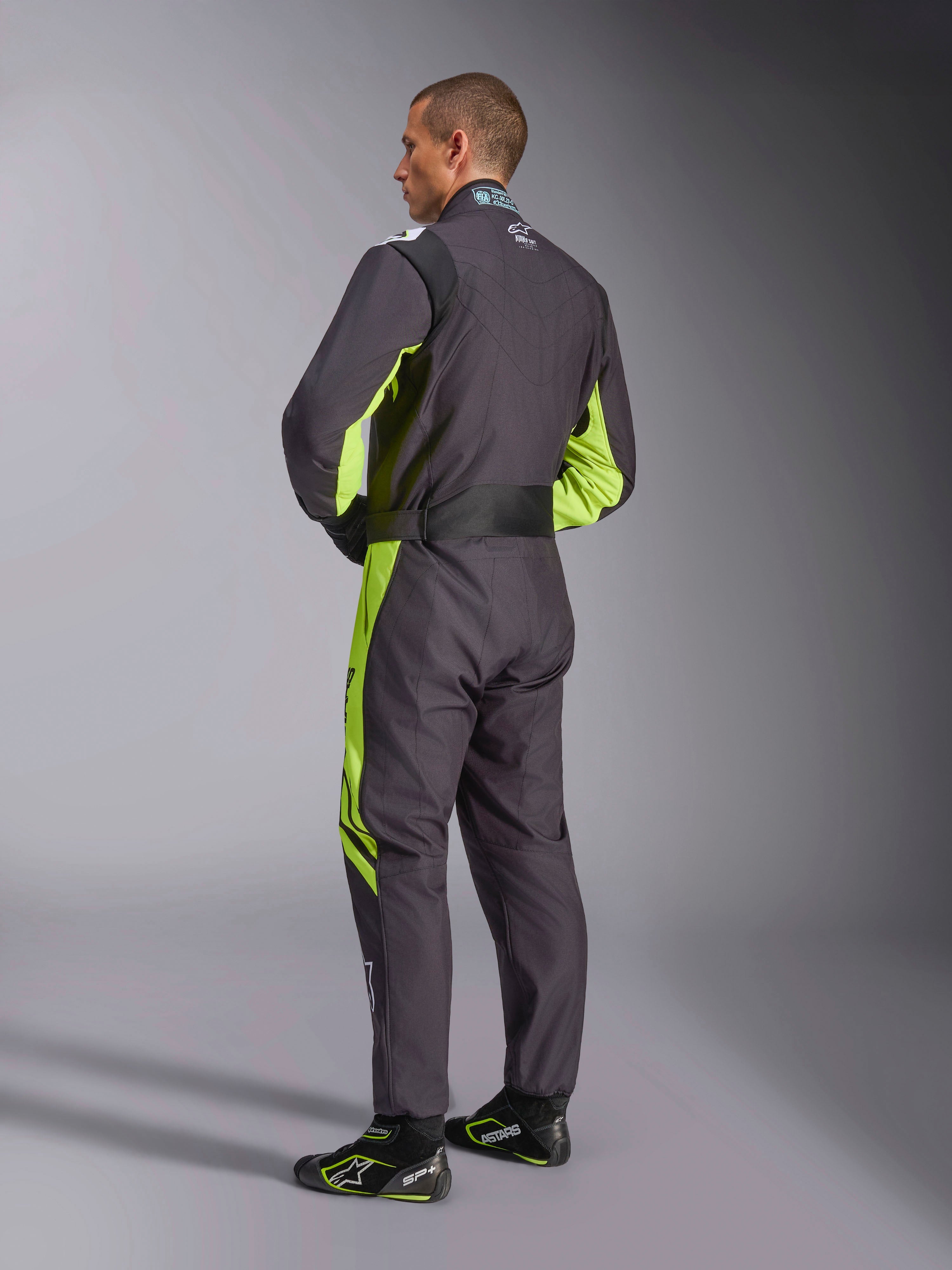 Alpinestars KMX-9 V3 Graphic 3 Suit, kombinezon kartingowy, czarno-żółty fluorescencyjny, widok modelu od tyłu prezentujący jednoczęściową konstrukcję z fluorescencyjnymi żółtymi akcentami po bokach i pod pachami, ergonomiczne elastyczne panele w części lędźwiowej oraz regulowany pas w talii, zestawiony z pasującymi butami wyścigowymi.