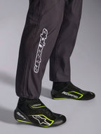 Alpinestars KMX-9 V3 Graphic 3 Suit, kombinezon kartingowy, czarny, zbliżenie na dolną część nogawek i mankiety przy kostkach, z białym pionowym logo Alpinestars, zestawiony z czarno-żółtymi (fluo) butami kartingowymi, detal profesjonalnej odzieży kartingowej.