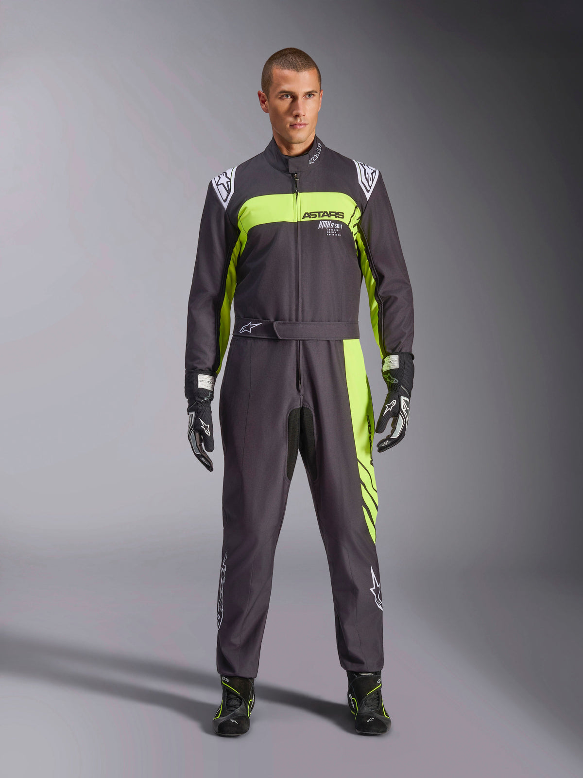 Alpinestars KMX-9 V3 Graphic 3 Suit, czarno-żółty fluo, profesjonalny jednoczęściowy kombinezon kartingowy prezentowany przez modela, z wyraźnymi neonowymi żółtymi akcentami, logo ASTARS na klatce piersiowej oraz pasującymi rękawicami i butami wyścigowymi.