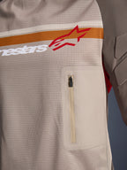 Alpinestars Maxdura Dual Jersey, Aluminum Walnut, zbliżenie na detale siatkowego korpusu, poziomy pomarańczowo-biały pas z czerwonym logo, pionowa kieszeń na piersi na zamek, odzież motocyklowa typu adventure