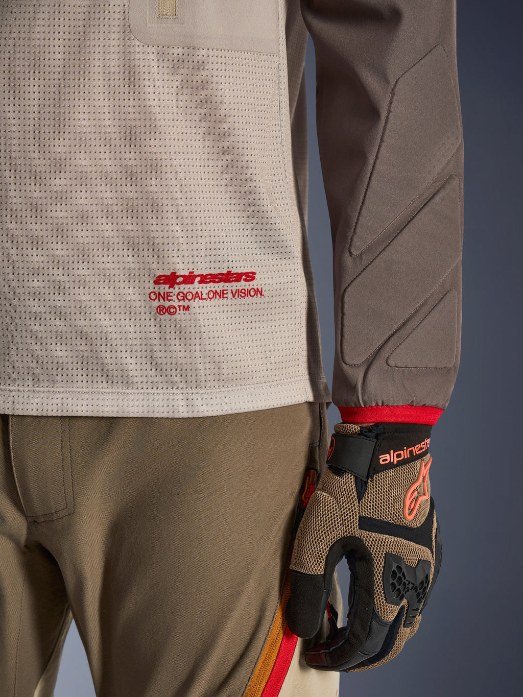 Alpinestars Maxdura Dual Jersey w kolorze Aluminum Walnut, widok szczegółowy pokazujący wentylowany siatkowy tors z czerwonym logo, rękaw odporny na ścieranie ze zintegrowanymi wyściółkami, noszona z dopasowanymi spodniami i rękawicami adventure