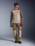 Alpinestars Maxdura Dual Jersey w kolorze Aluminum Walnut, koszulka motocyklowa adventure z beżowym siatkowym korpusem i brązowymi rękawami, z czerwonym kołnierzykiem i poziomym pasem na klatce piersiowej z logo Alpinestars, noszona z dopasowanymi spodniami adventure i rękawicami.