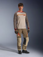 Model w koszulce Alpinestars Maxdura Dual Jersey w kolorze Aluminum Walnut, z szarym siatkowym torsem, brązowymi rękawami z czerwonymi mankietami i kieszeniami na klatce piersiowej na zamek, w stylizacji z pasującym sprzętem terenowym do jazdy adventure.