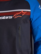 Alpinestars Maxdura Dual Jersey, zbliżenie na klatkę piersiową i rękaw, ciemnoszary i niebieski, zapinana na zamek kieszeń na piersi, oddychający siatkowy tułów, zintegrowane ochraniacze na rękawach, logo Alpinestars na tle czerwonych i białych pasów