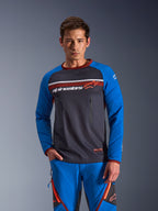 Mężczyzna w koszulce Alpinestars Maxdura Dual Jersey w kolorach Deep Gray i Royal Blue z pomarańczowymi akcentami, tors z pełnej siatki i zapinane kieszenie na klatce piersiowej, niebieskie spodnie adventure, techniczna odzież dual-sport i off-road