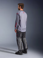 Man wearing Alpinestars Maxdura Dual Jersey, light gray with red Alpinestars logos, back view showing mesh torso and long sleeves, paired with charcoal technical pants and black motorcycle boots