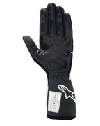 Rękawice Alpinestars Tech-1 Race V4, profesjonalne rękawice wyścigowe, czarno-szare (Black Tar Gray), widok od strony dłoni z silikonowym wzorem poprawiającym chwyt na palcach i wnętrzu dłoni, przedłużony mankiet z białym logo Alpinestars oraz certyfikatami FIA/SFI