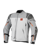 Kurtka Alpinestars Nazca 3L GORE-TEX PRO, motocyklowa kurtka adventure, ciemnoszara i szara z pomarańczowymi akcentami przy zamkach, logo All Terra na klatce piersiowej, wzmocnienia Superfabric na ramionach i łokciach, liczne otwory wentylacyjne zapinane na zamek, wytrzymały design turystyczny