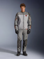 Kurtka Alpinestars Nazca 3L GORE-TEX PRO, motocyklowa kurtka adventure, kolor ciemnoszary i średnioszary, prezentowana przez modela z pasującymi spodniami i czarnymi rękawicami, pomarańczowe akcenty przy zamkach i czerwone logo na piersi, techniczna odzież ochronna do ekstremalnej jazdy