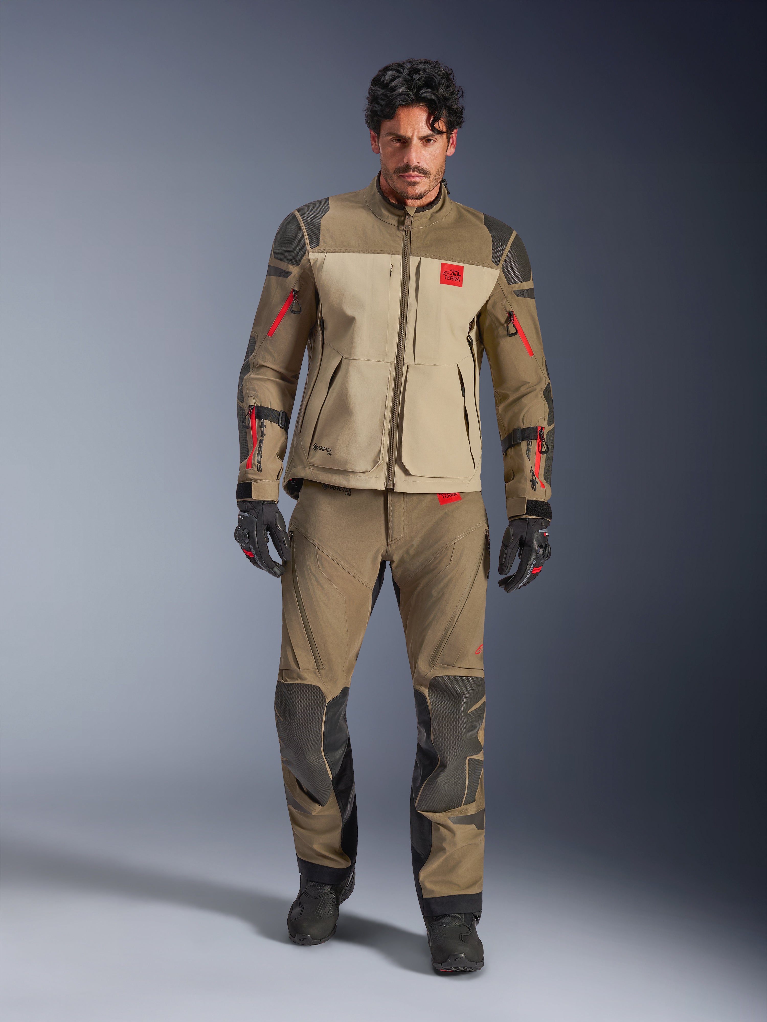 Kurtka Alpinestars Nazca 3L GORE-TEX PRO, Walnut Rock Brown, motocyklowa kurtka przygodowa noszona z dopasowanymi spodniami i rękawicami, czerwone akcenty na zamkach, logo „All Terra” na piersi, wytrzymała konstrukcja tekstylna